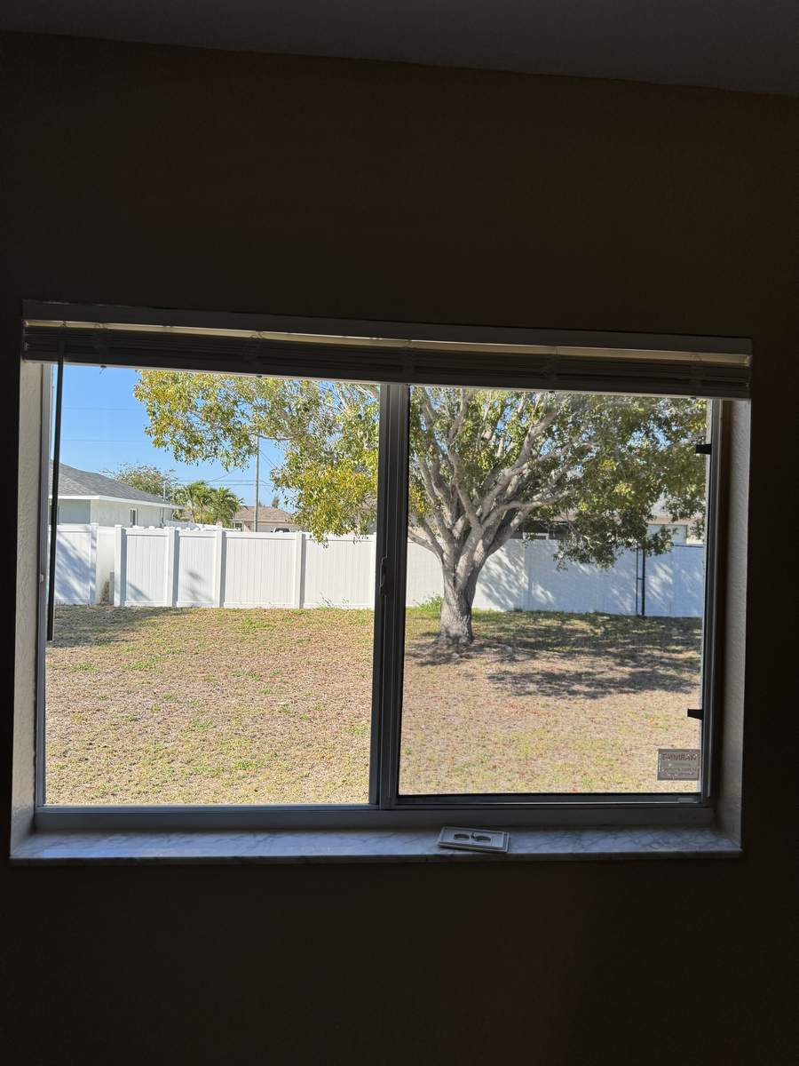 Clean sliding window looking out onto a fenced backyard and shade tree in Cape Coral, Florida
